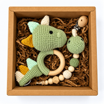 Sage green crochet dinosaur baby rattle and matching dinosaur pacifier holder in a kraft gift box