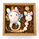 Handmade crochet unicorn baby rattle and matching unicorn pacifier holder in a kraft gift box